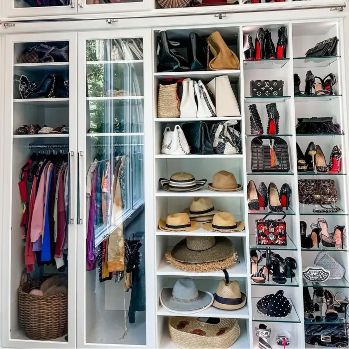 custom closet with glass doors, white shelves, glass shelves, hanging clothes, shoes, hats and handbags
