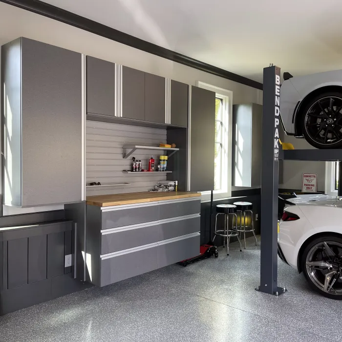 Modern garage with custom gray storage cabinets, workbench and two white corvette cars.
