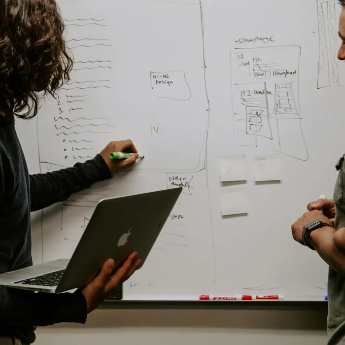 Two professionals collaborating and brainstorming ideas on a whiteboard with notes and sketches