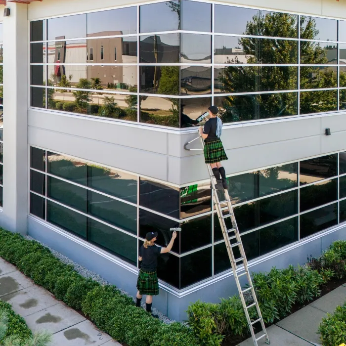 a couple of people washing windows on a ladder outside a building