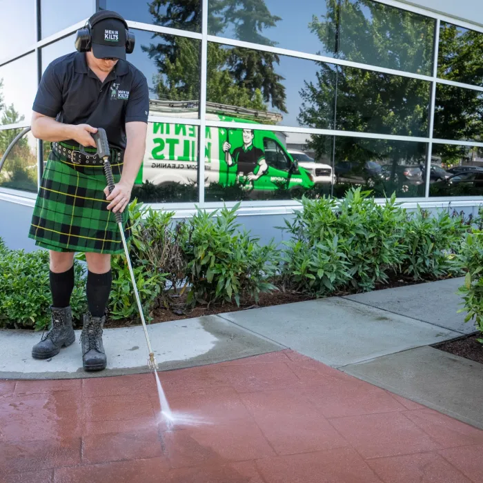 a man in a kilt pressure washing a sidewalk