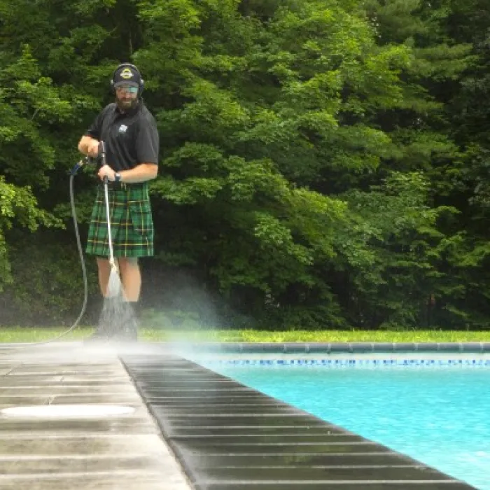 a man standing next to a pool washing the pool deck