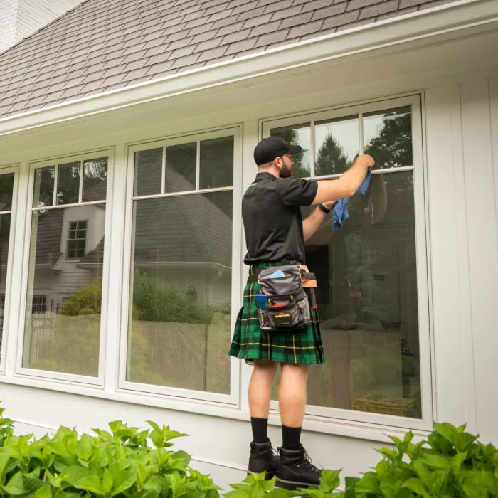 a person wearing a kilt and washing a window on a house