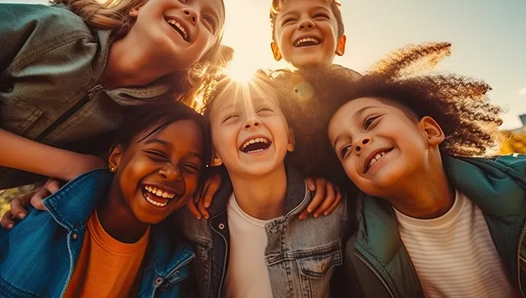 Group of five diverse children laughing and enjoying a sunny outdoor moment together in a close huddle.