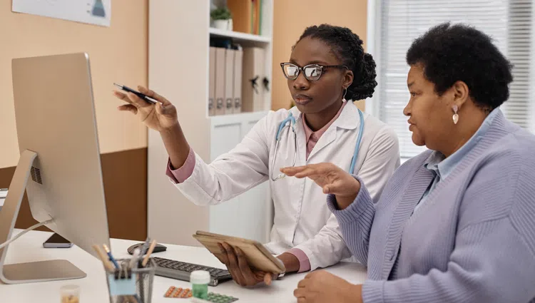 Female doctor with stethoscope explaining medical information to a middle-aged woman using a computer.