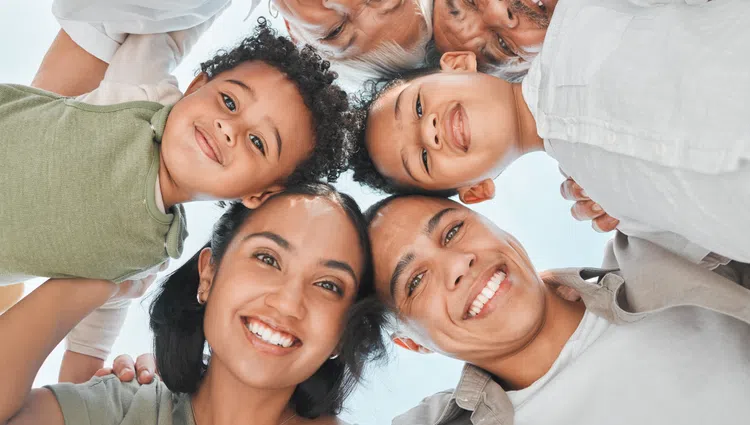 Happy multigenerational family smiling in a circle looking down at the camera outdoors on a sunny day.