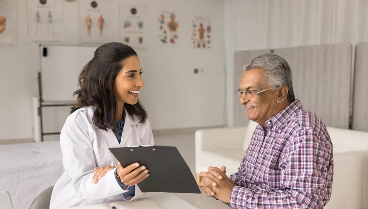 Doctor smiling and consulting with senior male patient in a medical office, discussing health information.