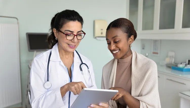 Female doctor in white coat showing tablet to smiling patient in medical exam room