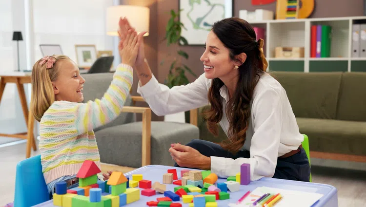 Smiling woman and young girl giving a high five while playing with colorful building blocks at a table.