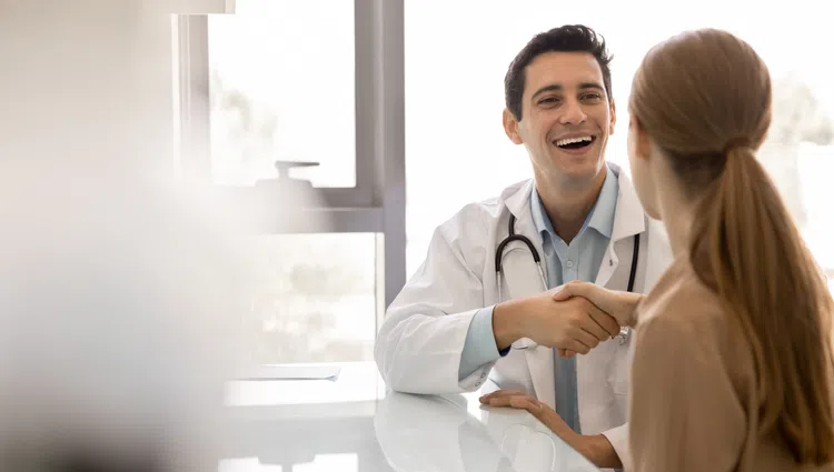Doctor smiling and shaking hands with patient during medical consultation in bright office.