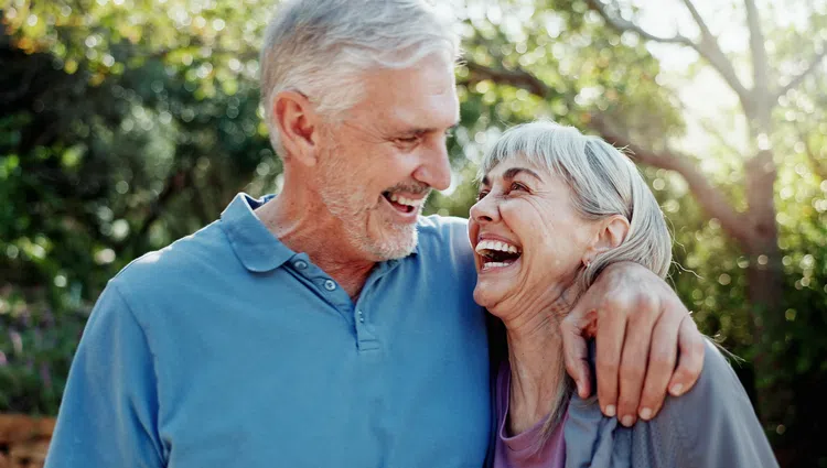 Happy elderly couple smiling and embracing outdoors with sunlight and greenery in the background