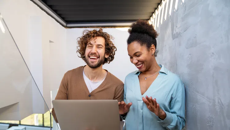 Happy young man and woman looking at laptop screen and sharing a laugh together indoors