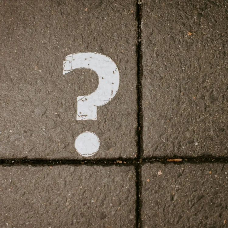 White question mark painted on dark textured pavement tiles divided by grout lines.