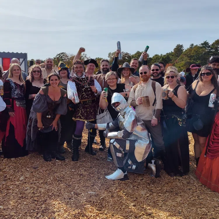 Large group of people in Renaissance costumes at an outdoor pub crawl event on a sunny day.