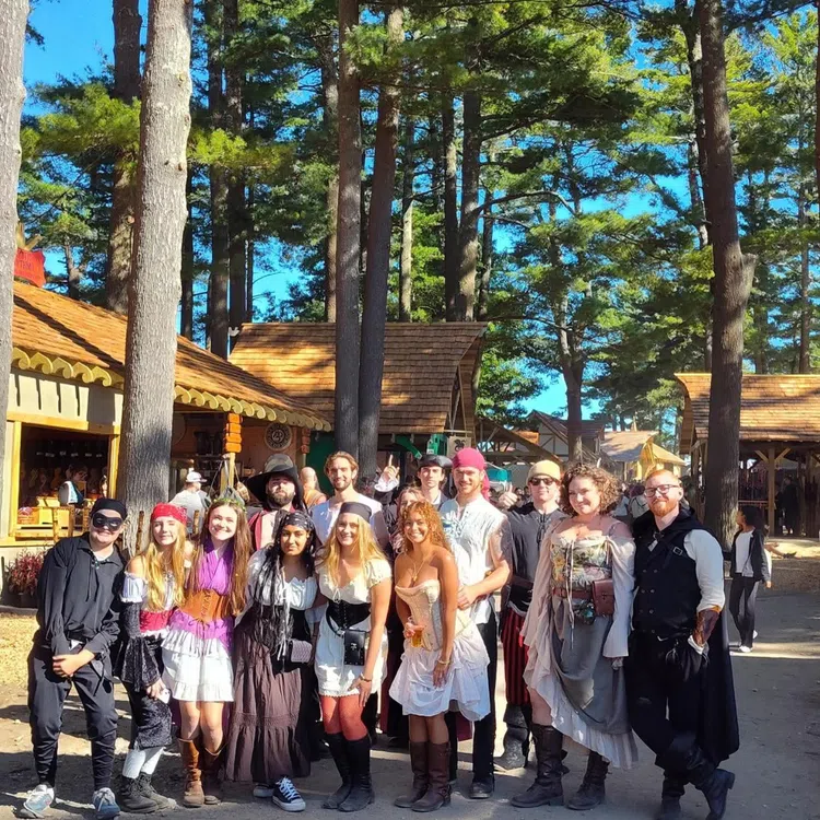 Group of people dressed in medieval and pirate costumes at an outdoor Renaissance fair on a sunny day.