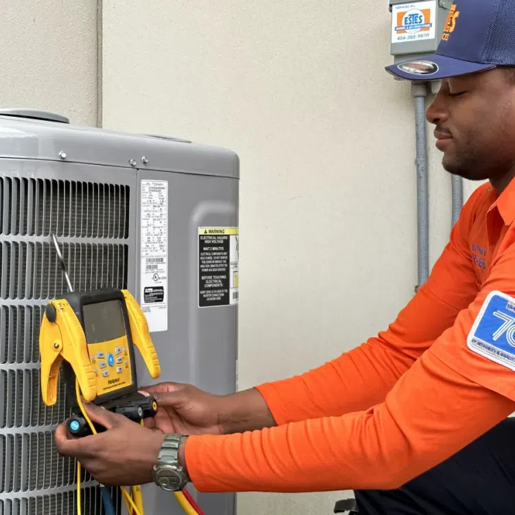 Technician in orange uniform testing a Carrier air conditioning unit with diagnostic equipment against a beige wall.