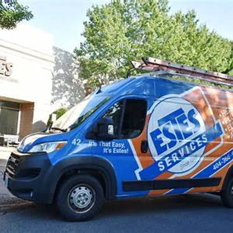 Blue and orange Estes Services van parked outdoors with ladder on top and company logo on side.