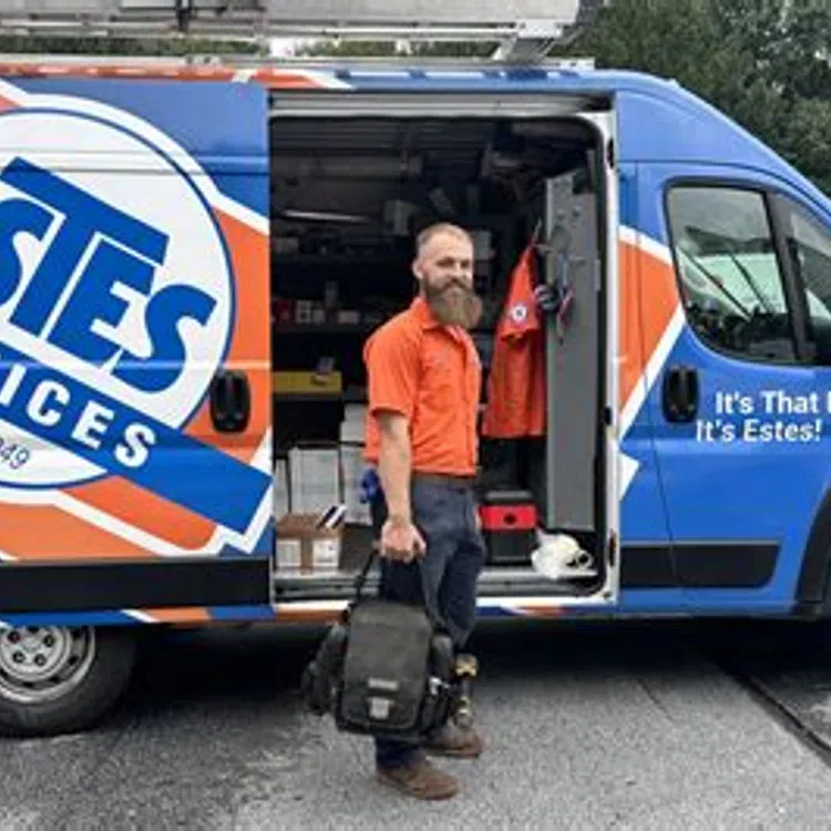 Estes Services technician standing outside branded service van holding bag ready for work outdoors.