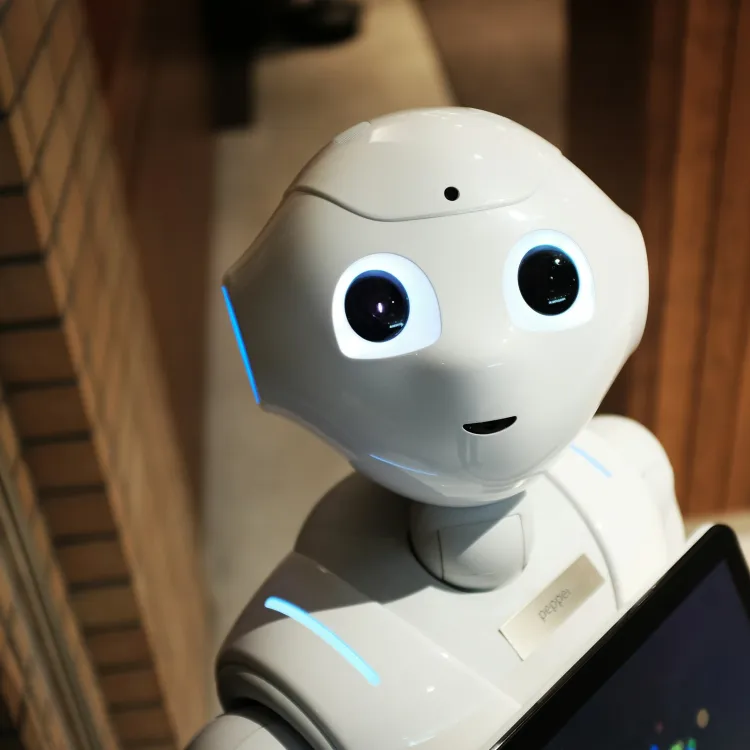 Friendly white humanoid robot with large expressive eyes holding a tablet in indoor setting with warm lighting.