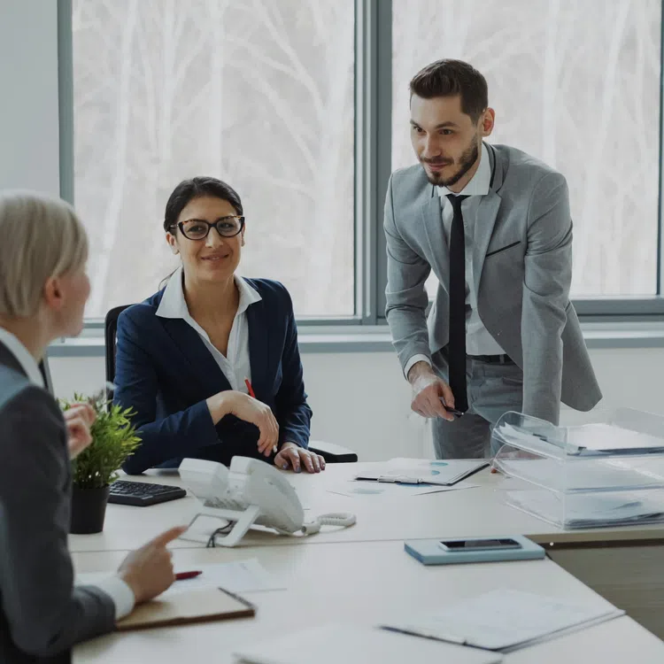 Four business professionals collaborating in a modern office with large windows and paperwork on the table.