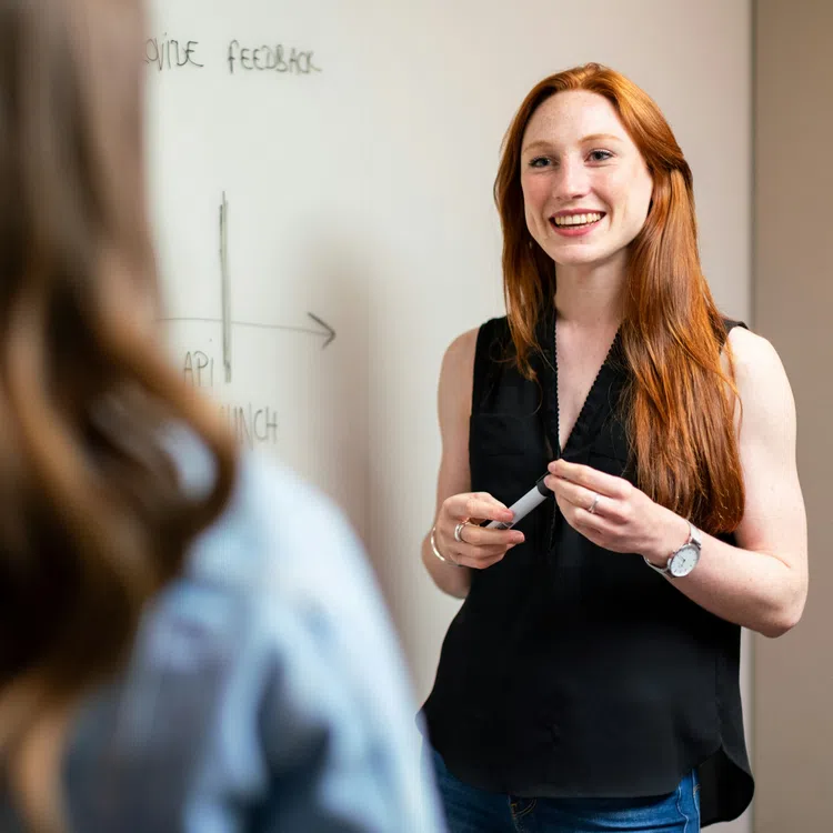 Smiling woman presenting ideas on a whiteboard during a meeting with a colleague in a modern office.