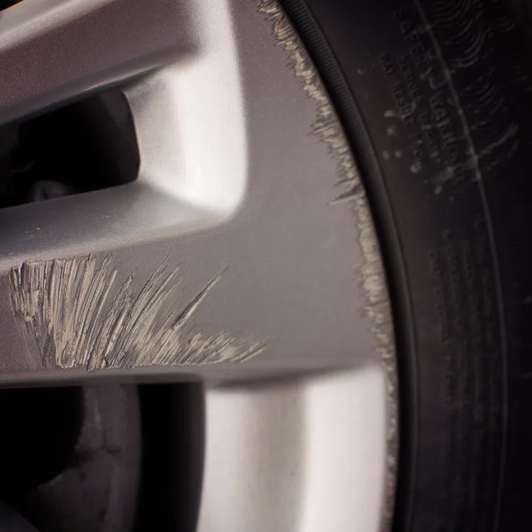 Close-up of a car wheel rim with visible curb rash scratches and damage on the metallic surface near the tire.