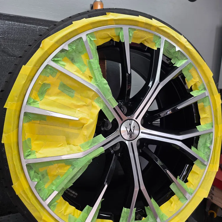 Maserati car rim partially masked with green and yellow tape for painting or protection.