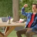 A man in a plaid shirt interacts with a miniature animated version of himself at a table.