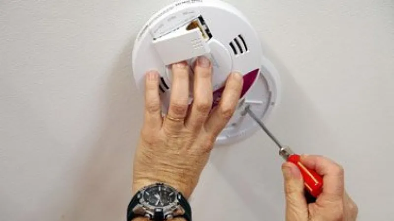 Person installing or repairing a smoke detector on a ceiling using a red screwdriver.