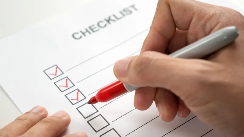 Person marking a checklist with red checkmarks on a white paper using a red pen.