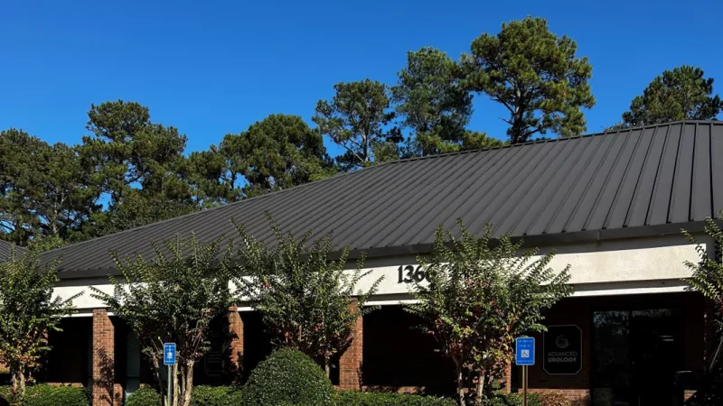 Modern medical office building with brick columns, dark roof, greenery, and clear blue sky on a sunny day.