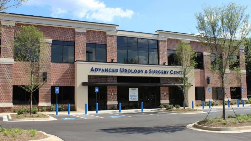Modern brick medical building with Advanced Urology & Surgery Center signage and parking lot with blue posts and trees.
