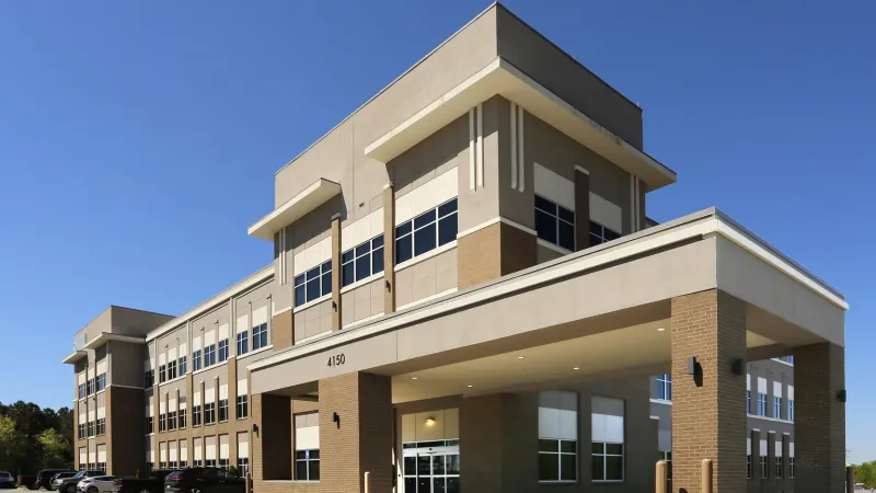 Modern three-story commercial office building with beige and brown facade under a clear blue sky.