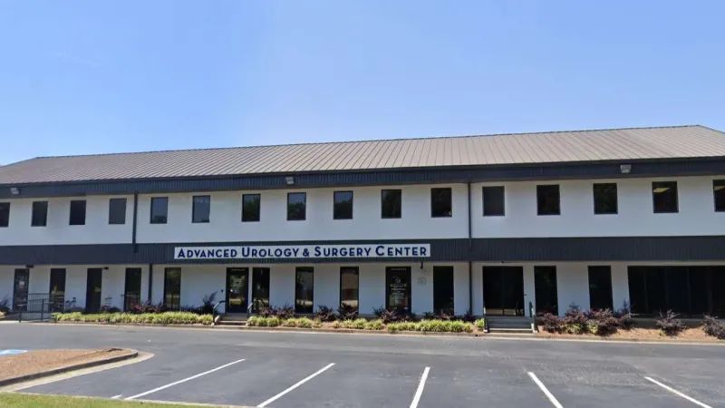 Modern two-story Advanced Urology & Surgery Center building with clear blue sky and empty parking lot in front.