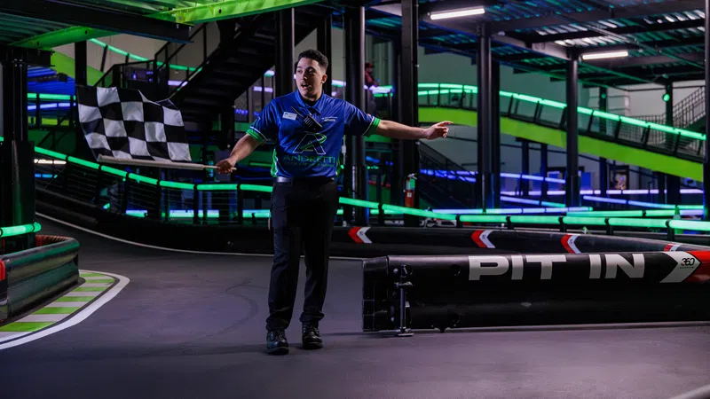 Race official waving a checkered flag at an indoor go-kart track with neon green and blue lighting.