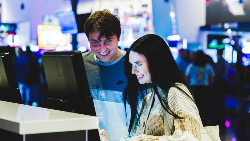 Young man and woman enjoying interactive touchscreen games in a vibrant arcade setting with colorful lights.