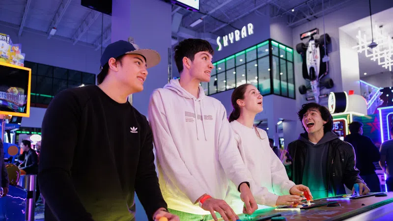 Four friends playing arcade games together at a vibrant indoor entertainment center called Skybar.