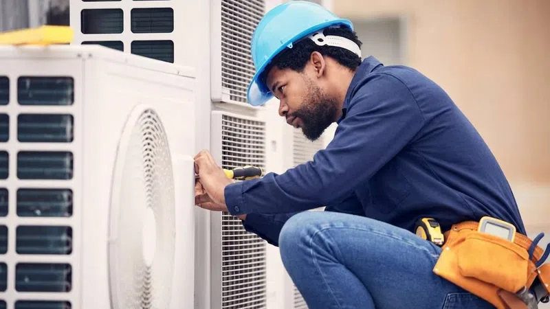Badger Bob's local AC Repair technician in blue hard hat repairing air conditioning unit outdoors with tool belt and focused expression