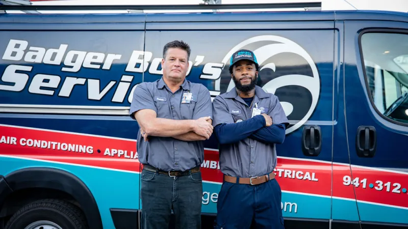 Two uniformed technicians standing confidently in front of a Badger Boy's Service van with tools and ladder.