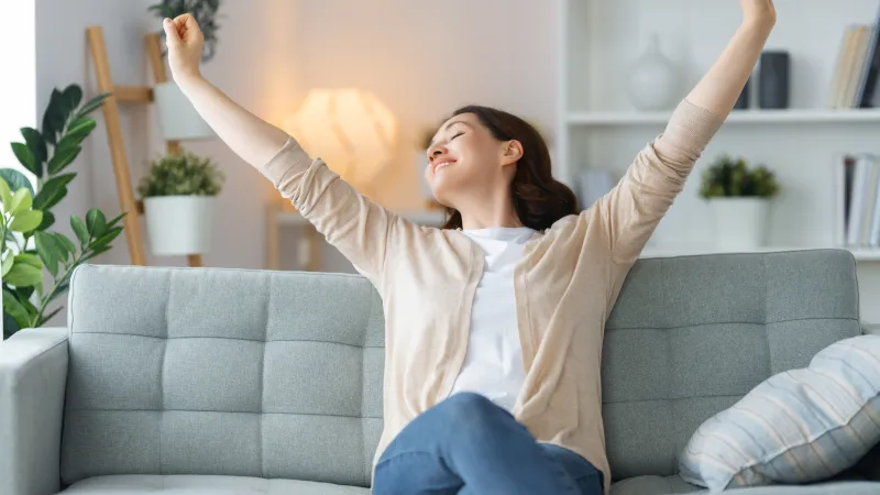 A woman enjoying relaxation on a couch, stretching with a joyful expression in a cozy living room setting.
