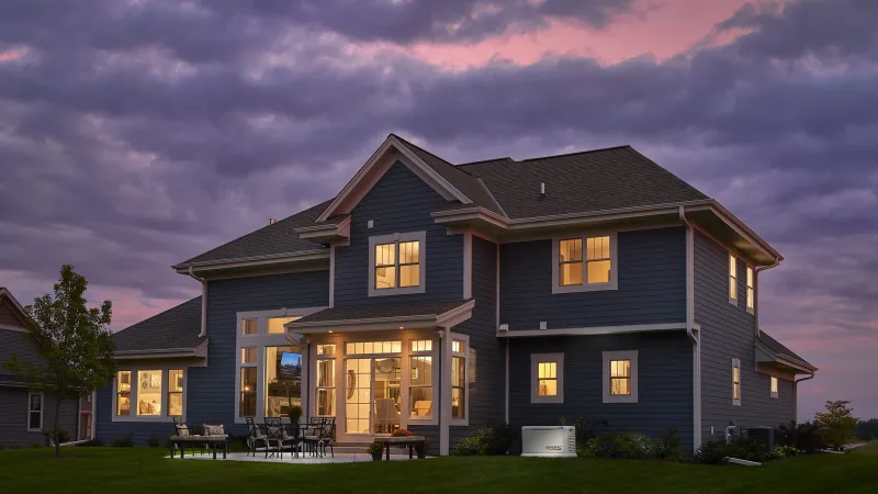 Blue two-story house with warm interior lights and cloudy purple sunset sky in the background