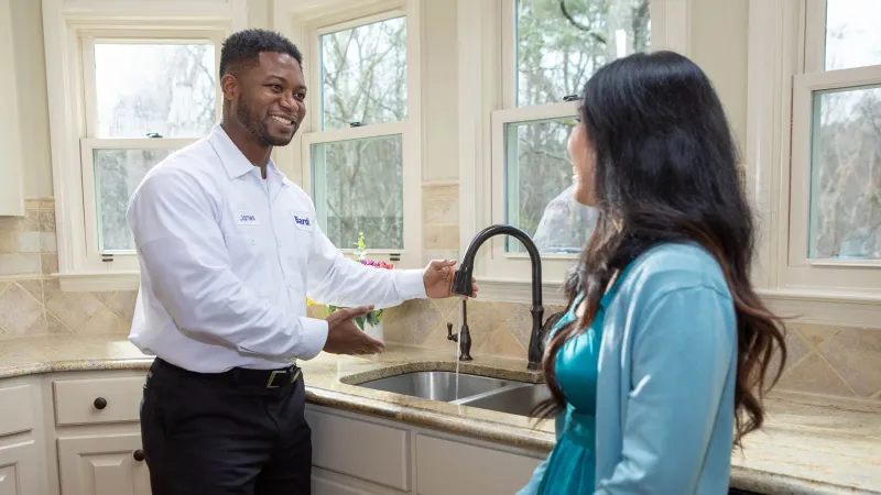 A plumber demonstrates a kitchen faucet is working and draining to a customer.