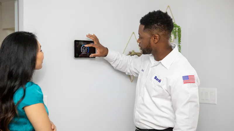 Technician adjusts a smart thermostat while discussing options with a homeowner in a modern setting.