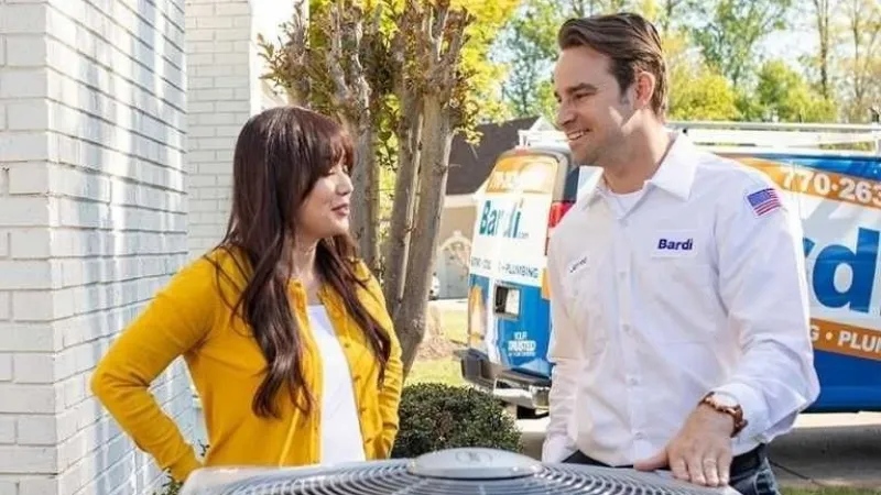 HVAC technician talking to homeowner near air conditioning unit outside a house on a sunny day.