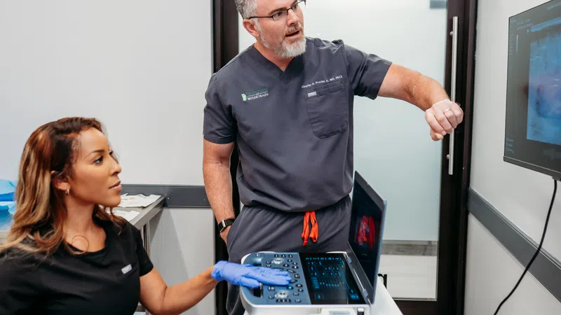 Doctor explains ultrasound results to patient using medical imaging equipment in clinic room