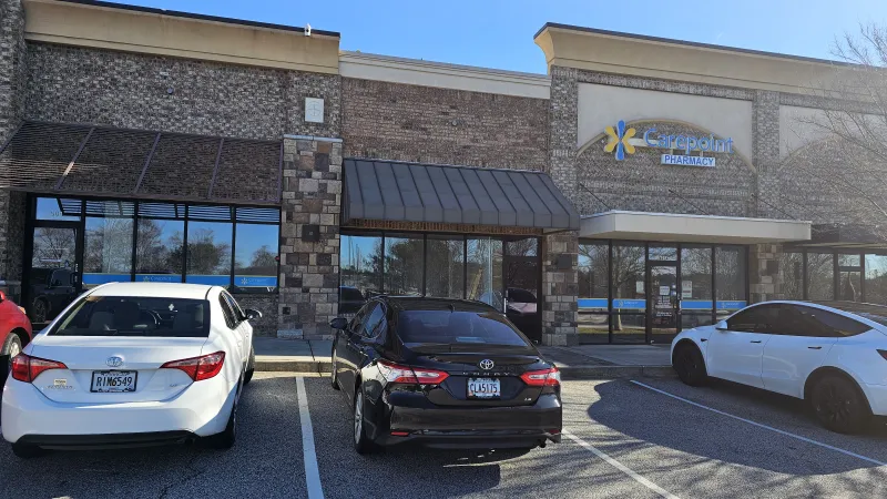 Front view of Carepoint Pharmacy with three cars parked outside in a strip mall on a sunny day.