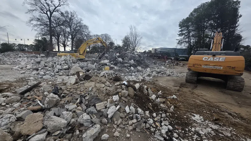 Construction site with excavators and rubble piles under a cloudy sky during demolition work.
