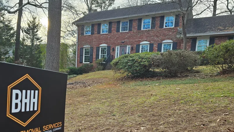 Two-story brick house with black shutters and BHH Demolition & Removal Services sign in front yard