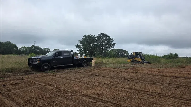 Black pickup truck and compact loader parked on a freshly tilled dirt field under cloudy sky