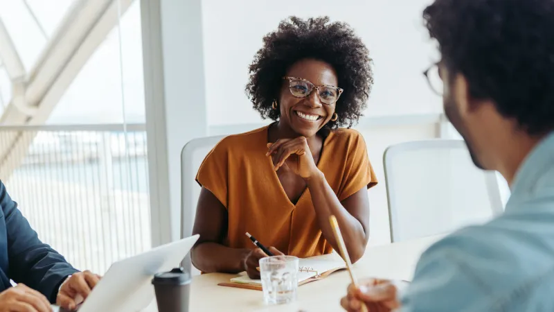 Smiling woman in glasses leads discussion with colleagues in bright modern office during meeting.